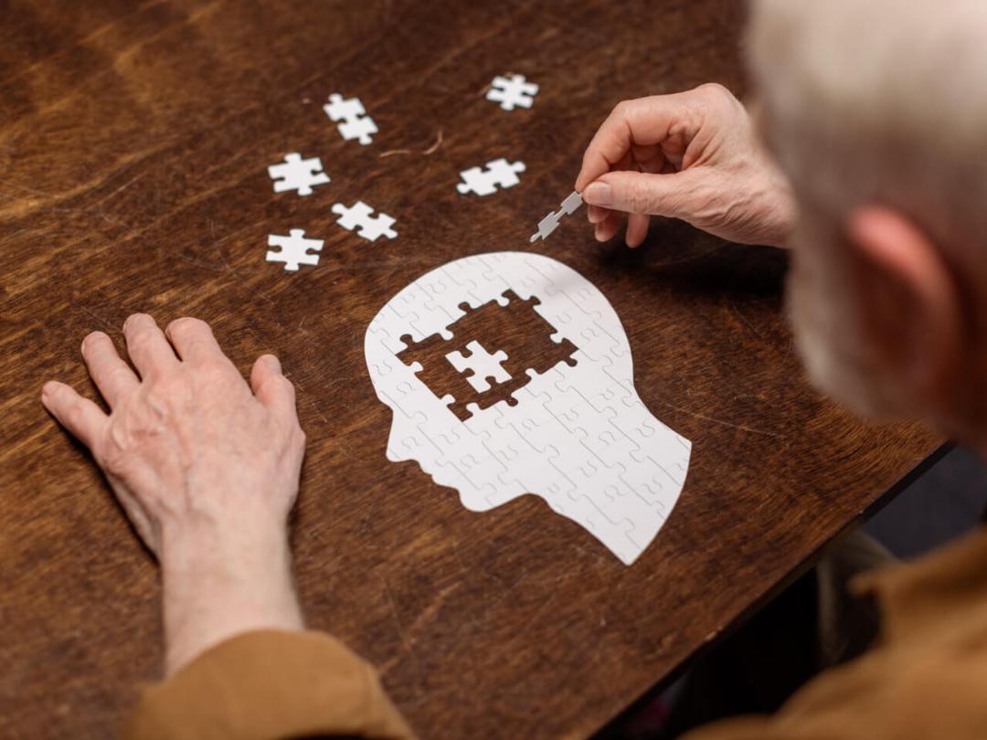 Hochwinkelansicht eines älteren Mannes, der Puzzles als Demenz-Reha sammelt.