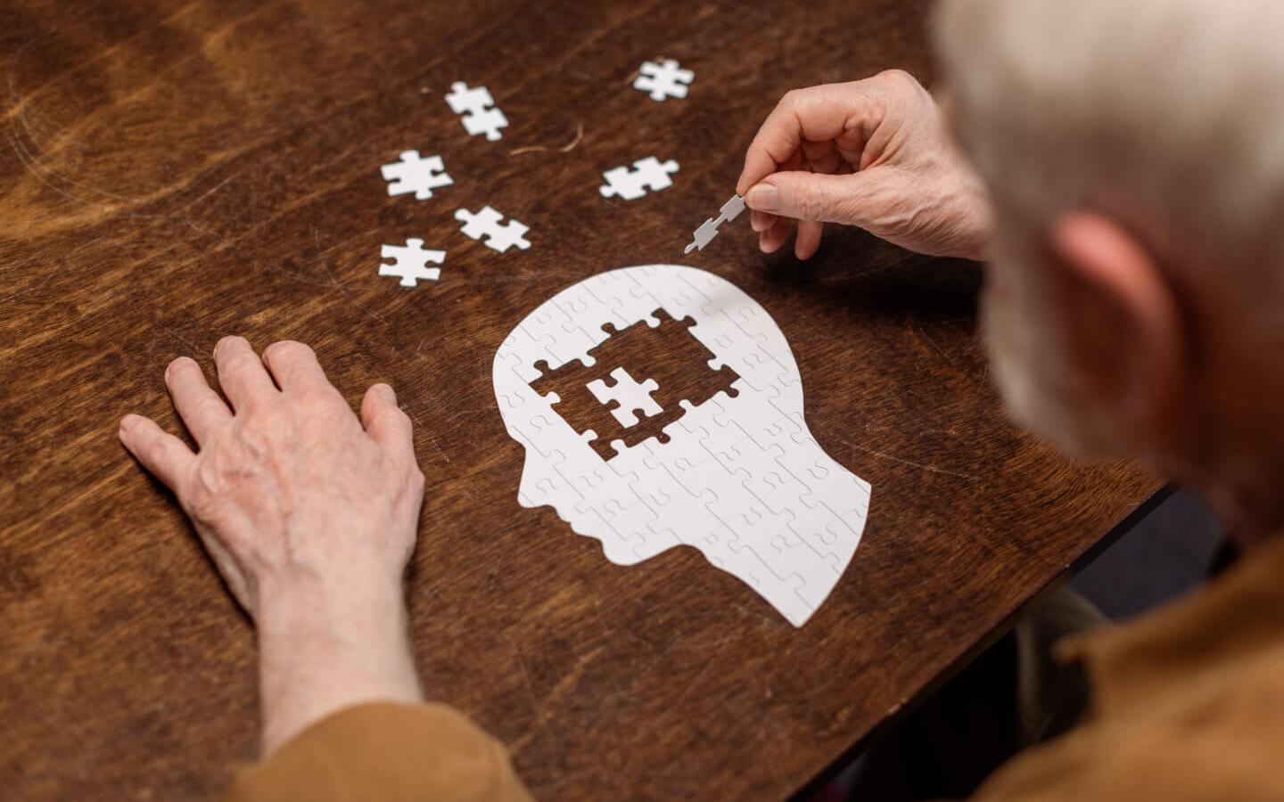 Hochwinkelansicht eines älteren Mannes, der Puzzles als Demenz-Reha sammelt.