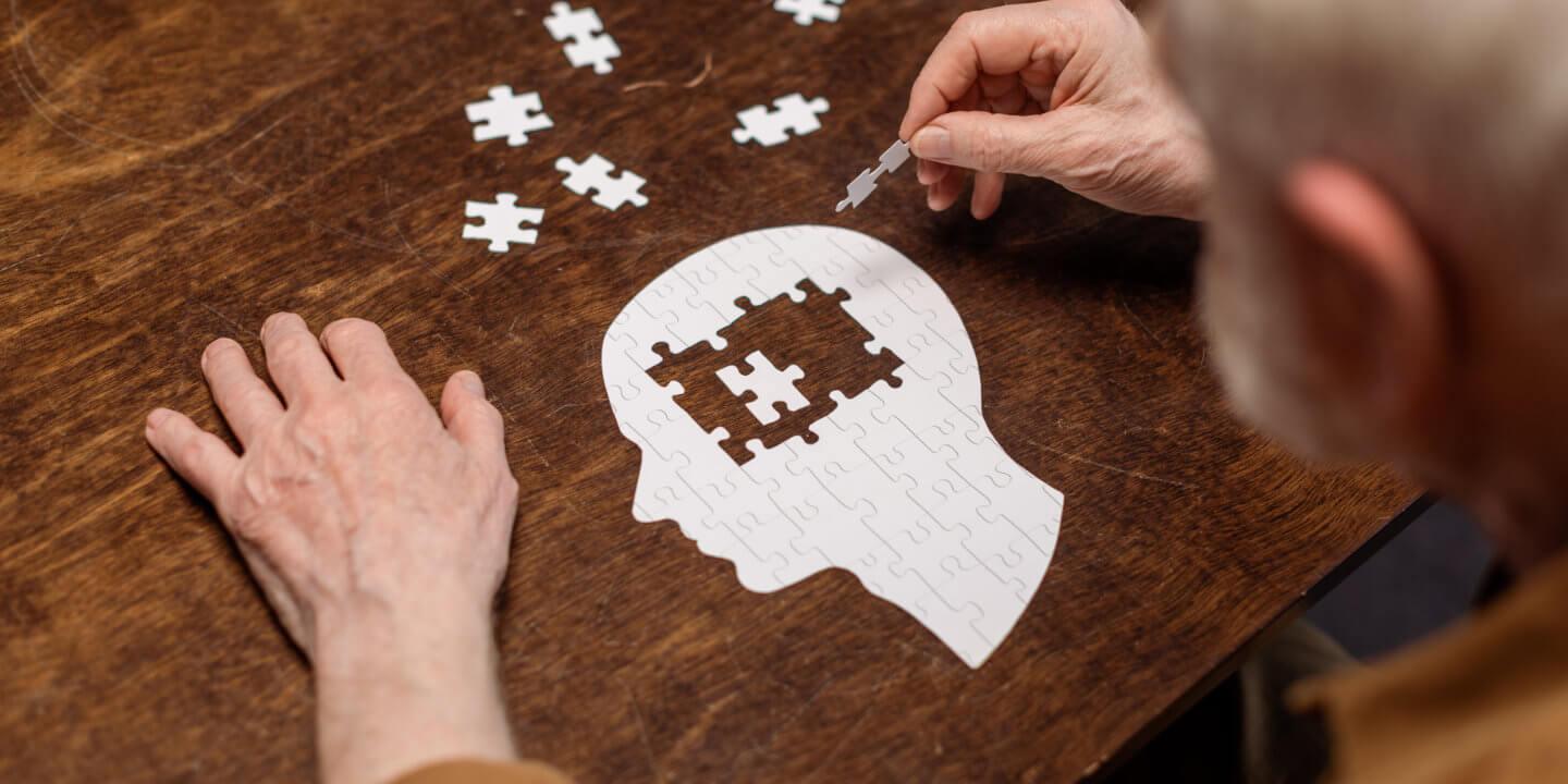 Hochwinkelansicht eines älteren Mannes, der Puzzles als Demenz-Reha sammelt.