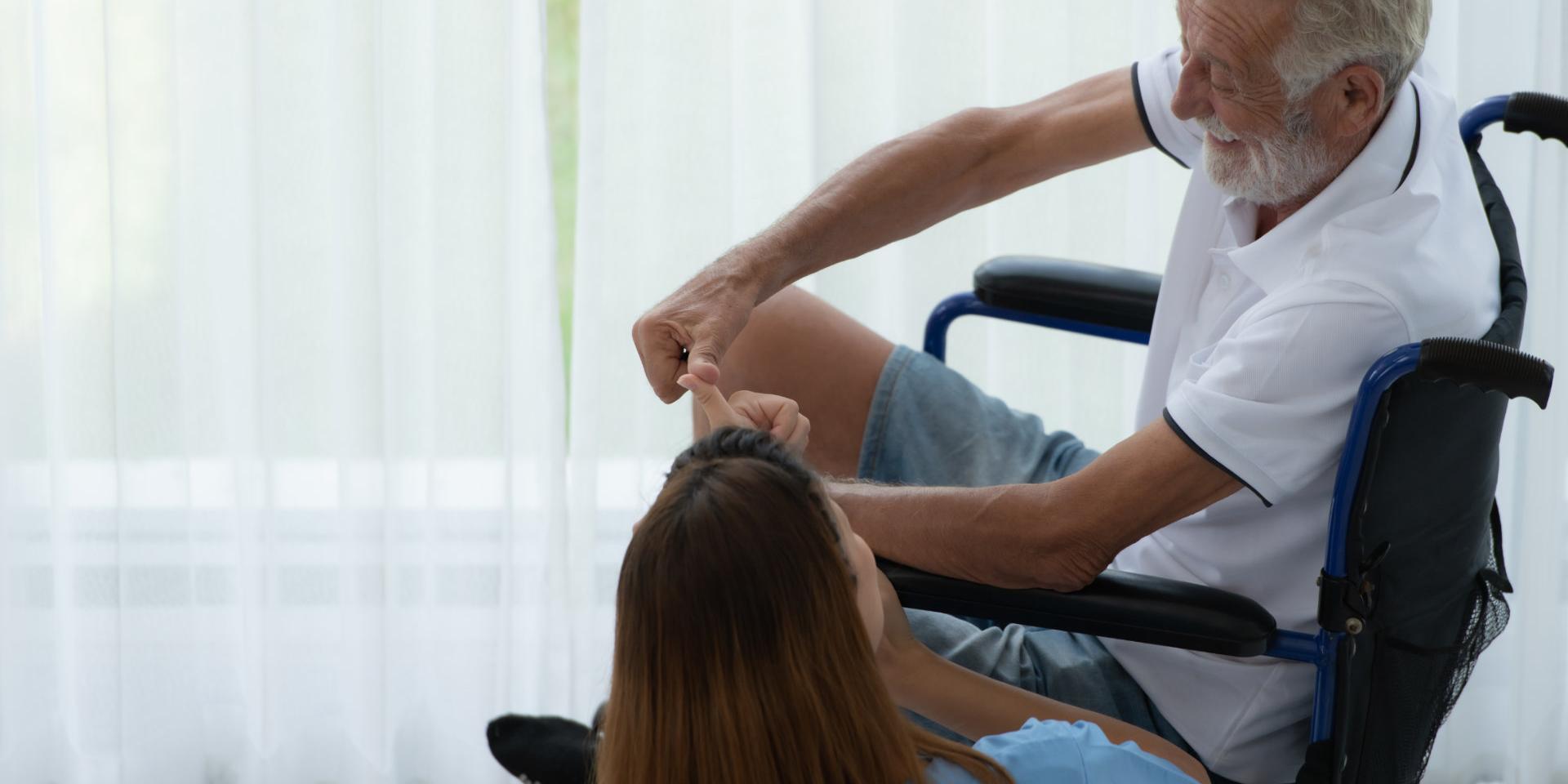 Haushaltshilfe unterhält sich mit pflegebedürftigem Senior im Rollstuhl