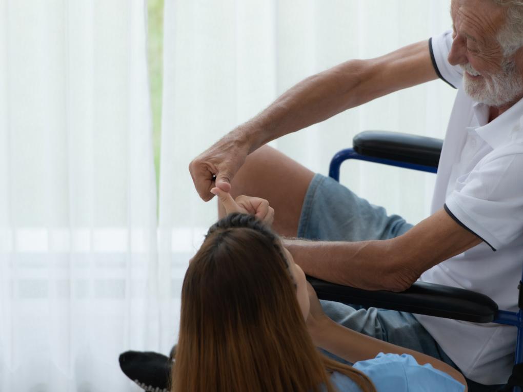 Haushaltshilfe unterhält sich mit pflegebedürftigem Senior im Rollstuhl