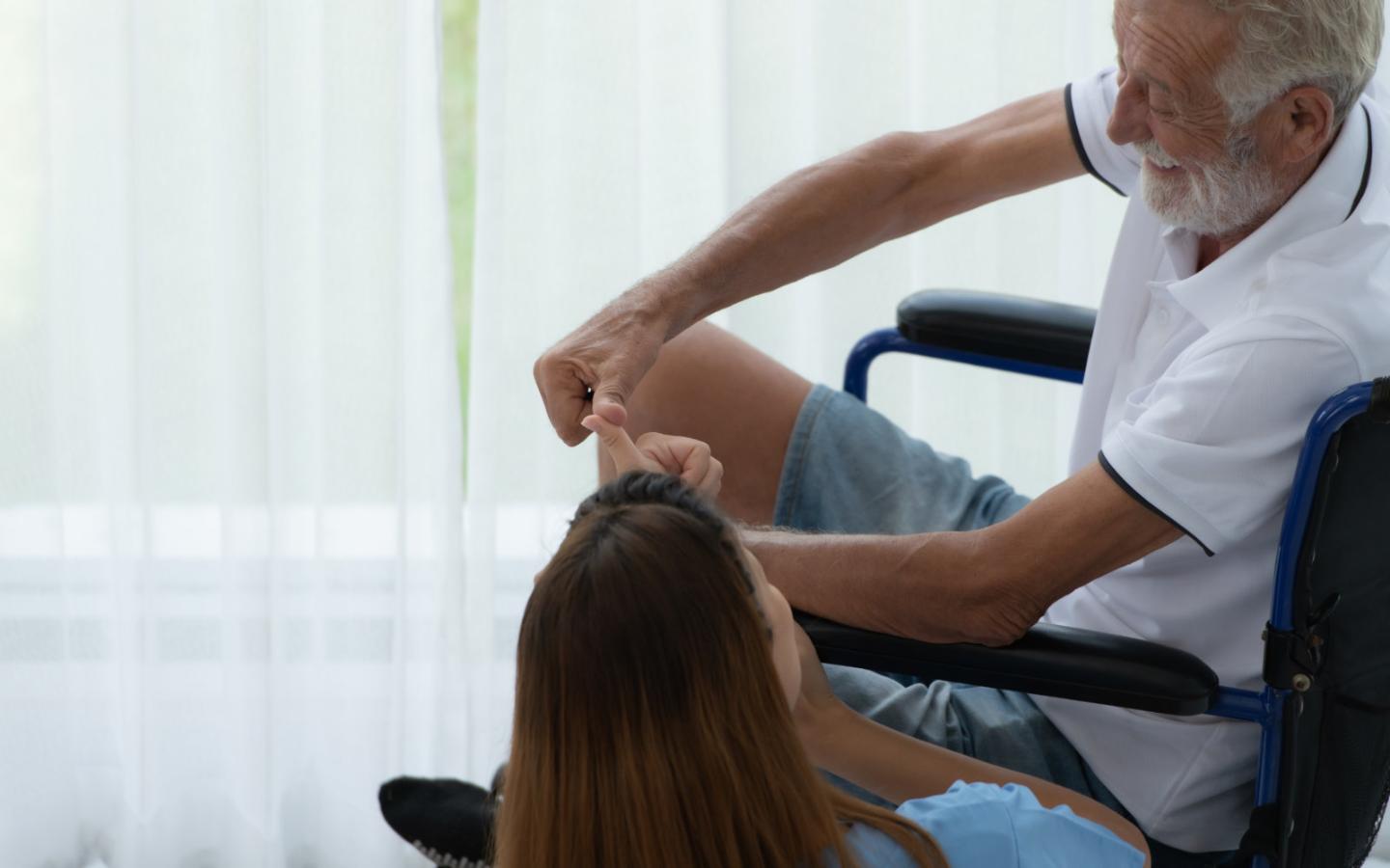Haushaltshilfe unterhält sich mit pflegebedürftigem Senior im Rollstuhl