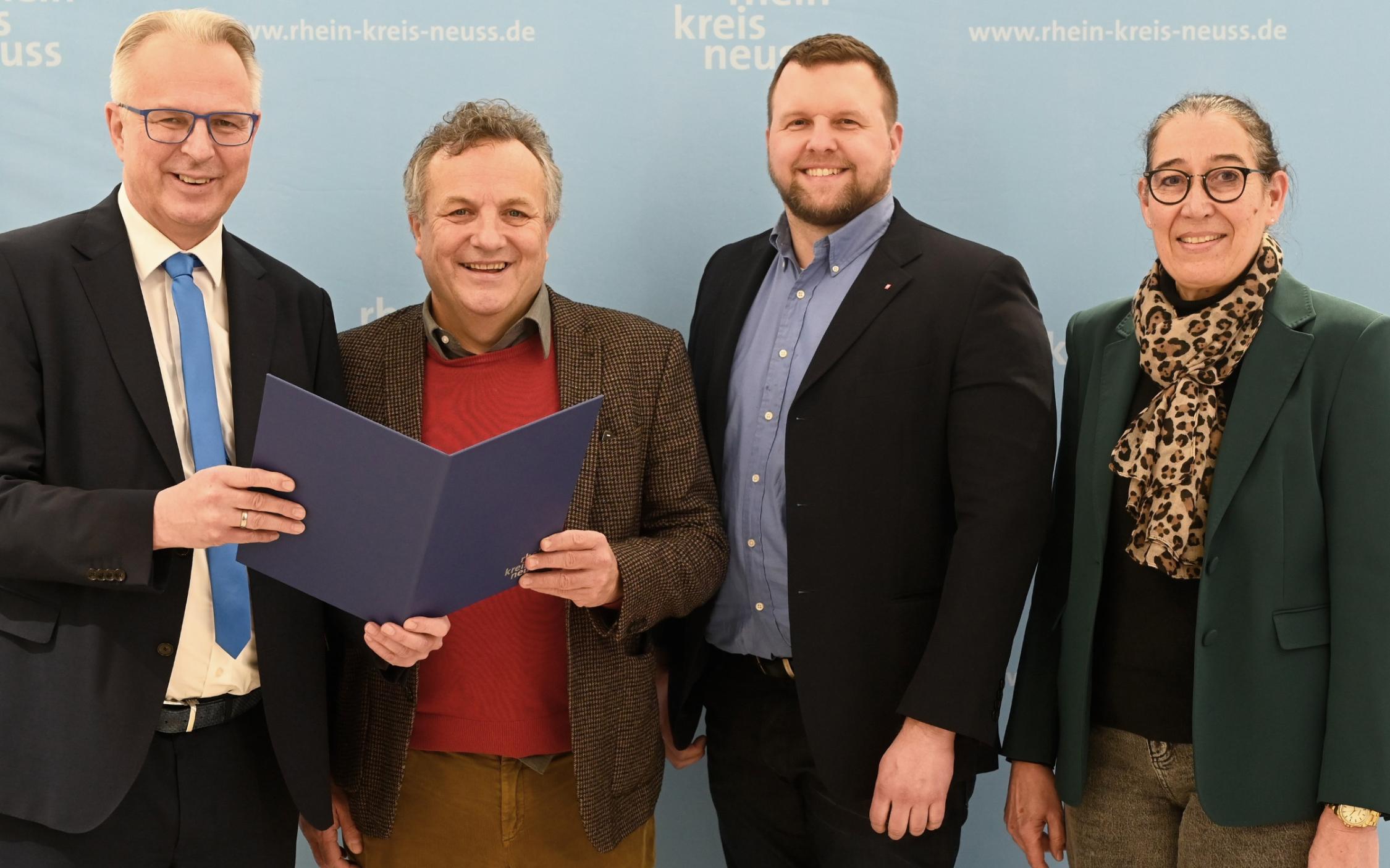 Kreisdirektor Dirk Brügge (links) übergibt dem Caritas-Vorstandsvorsitzenden Hermann Josef Thiel im Grevenbroicher Ständehaus den Zuwendungsbescheid 2025. Rechts Ulrike Weyerstraß, Leitung Kommunales Integrationszentrum Rhein-Kreis Neuss, daneben Caritas-Vorstand Benjamin Lampa.