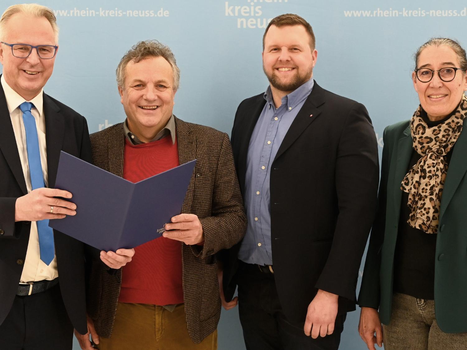 Kreisdirektor Dirk Brügge (links) übergibt dem Caritas-Vorstandsvorsitzenden Hermann Josef Thiel im Grevenbroicher Ständehaus den Zuwendungsbescheid 2025. Rechts Ulrike Weyerstraß, Leitung Kommunales Integrationszentrum Rhein-Kreis Neuss, daneben Caritas-Vorstand Benjamin Lampa.