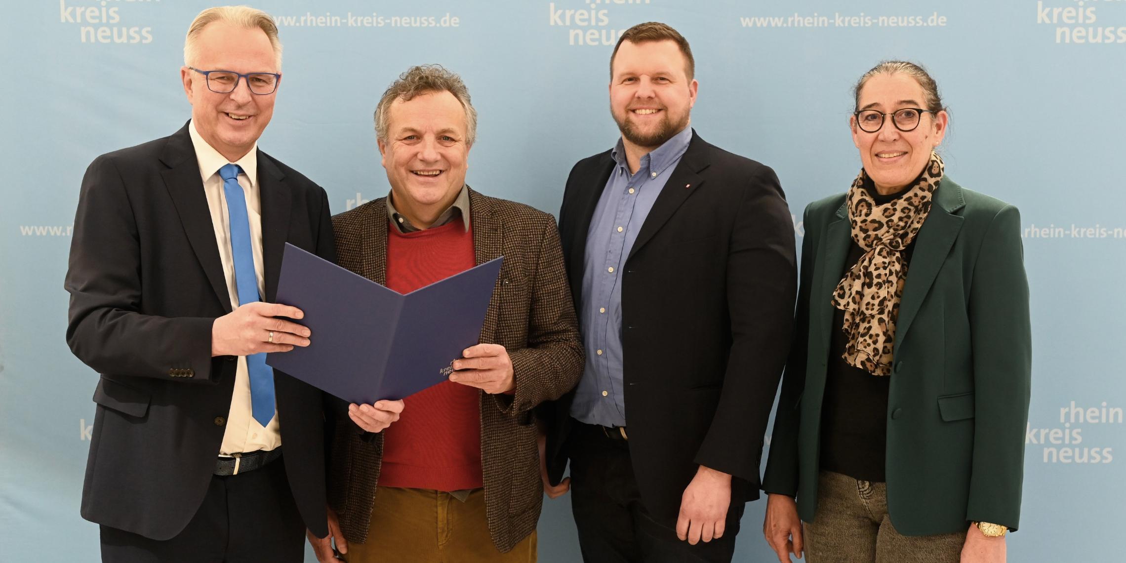 Kreisdirektor Dirk Brügge (links) übergibt dem Caritas-Vorstandsvorsitzenden Hermann Josef Thiel im Grevenbroicher Ständehaus den Zuwendungsbescheid 2025. Rechts Ulrike Weyerstraß, Leitung Kommunales Integrationszentrum Rhein-Kreis Neuss, daneben Caritas-Vorstand Benjamin Lampa.