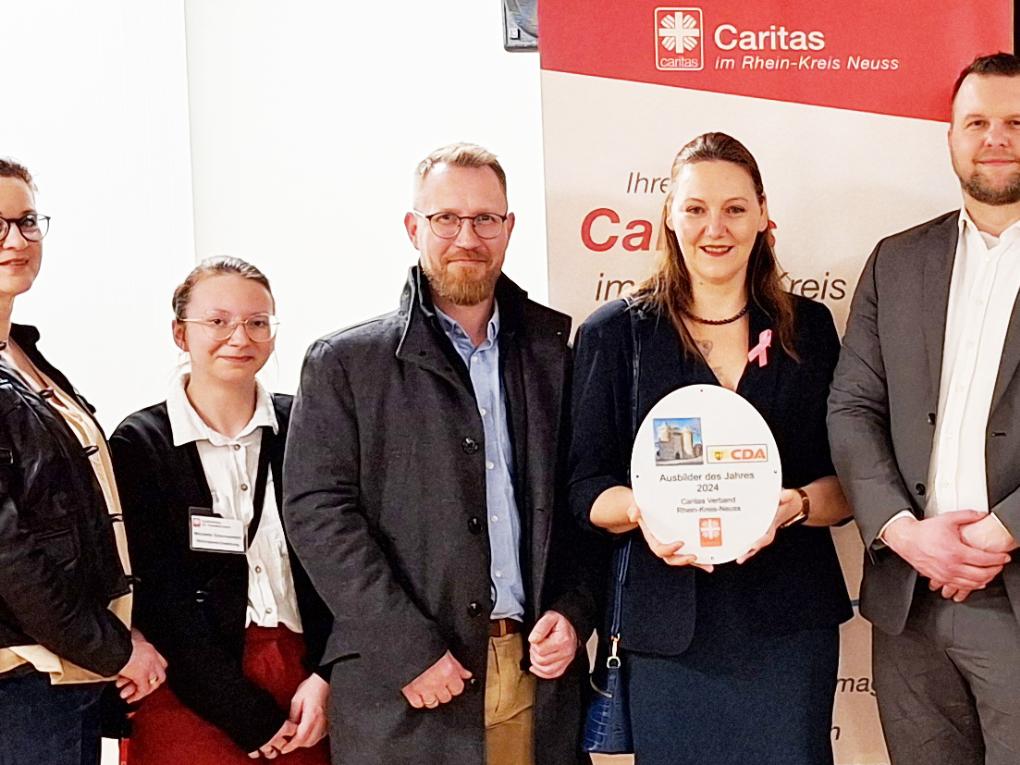 Stolz hält die freigestellte Praxisanleiterin Katrin Titel den CDA-Preis „Bester Ausbildungsbetrieb im Rhein-Kreis Neuss“  in Händen. Rechts neben ihr Caritas-Vorstand Benjamin Lampa und die CDA-Vorstände Karin Kilb, Moderator Klaus de Nardo und Laudator Ralf Kruska. Links neben Katrin Titel stehen freigestellter Praxisanleiter Daniel Vogt, die ehemalige freigestellte Praxisanleiterin Michelle Dobrowolski (heute Wohnbereichsleitung Theresienheim) und Praxisanleiterin Tanja Milutinovic.