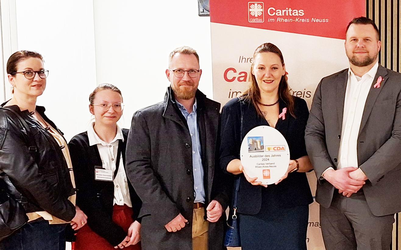 Stolz hält die freigestellte Praxisanleiterin Katrin Titel den CDA-Preis „Bester Ausbildungsbetrieb im Rhein-Kreis Neuss“  in Händen. Rechts neben ihr Caritas-Vorstand Benjamin Lampa und die CDA-Vorstände Karin Kilb, Moderator Klaus de Nardo und Laudator Ralf Kruska. Links neben Katrin Titel stehen freigestellter Praxisanleiter Daniel Vogt, die ehemalige freigestellte Praxisanleiterin Michelle Dobrowolski (heute Wohnbereichsleitung Theresienheim) und Praxisanleiterin Tanja Milutinovic.