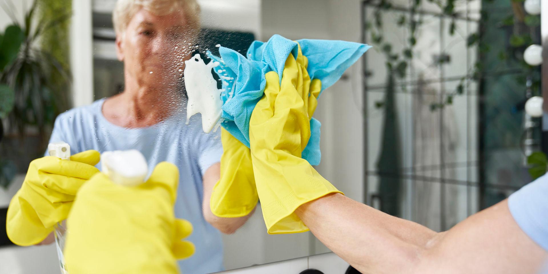 Haushaltshilfe putzt Spiegel bei einem Menschen, der über seinen Pflegegrad 1, die Haushaltshilfe über die Pflegekasse in Anspruch nimmt.