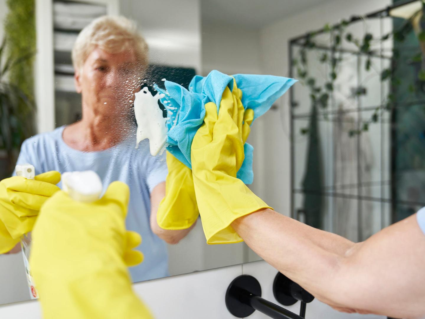 Haushaltshilfe putzt Spiegel bei einem Menschen, der über seinen Pflegegrad 1, die Haushaltshilfe über die Pflegekasse in Anspruch nimmt.